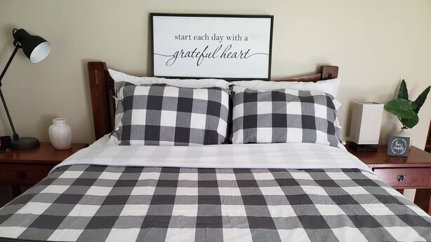 A neatly made bed with a checkered bedspread, a framed inspirational quote on the wall, and a bedside lamp. - Cozy Cabin In Roselle (Roselle)