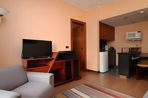 A modern living room with a flat-screen TV, a sofa, a wooden entertainment unit, and a kitchen area with a microwave. - OZPED Flats Particulares Bonaparte (Brasília)