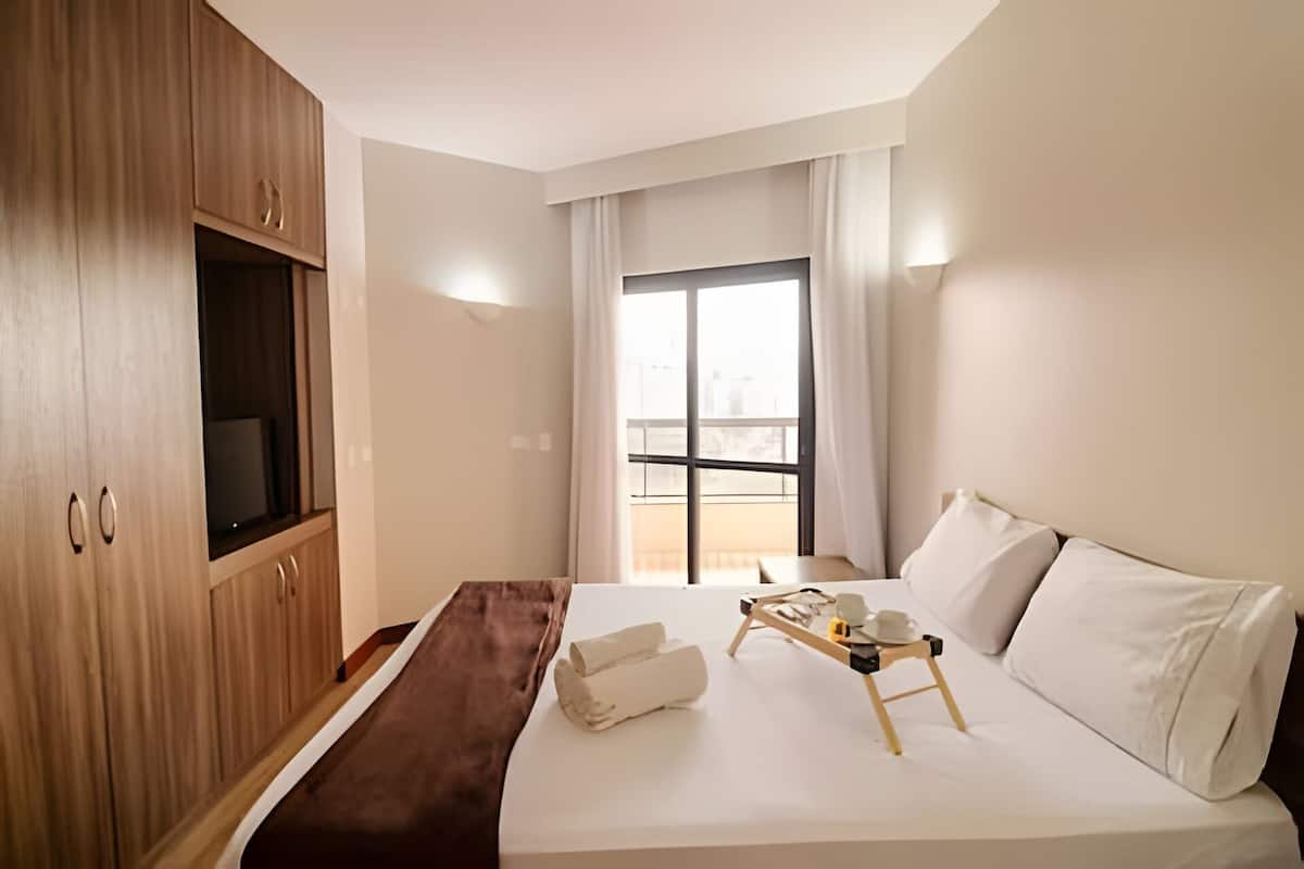 Ein Hotelzimmer mit einem Bett, einem Holzschrank, einem Fenster mit Vorhängen und einem kleinen Tisch mit Tablett.