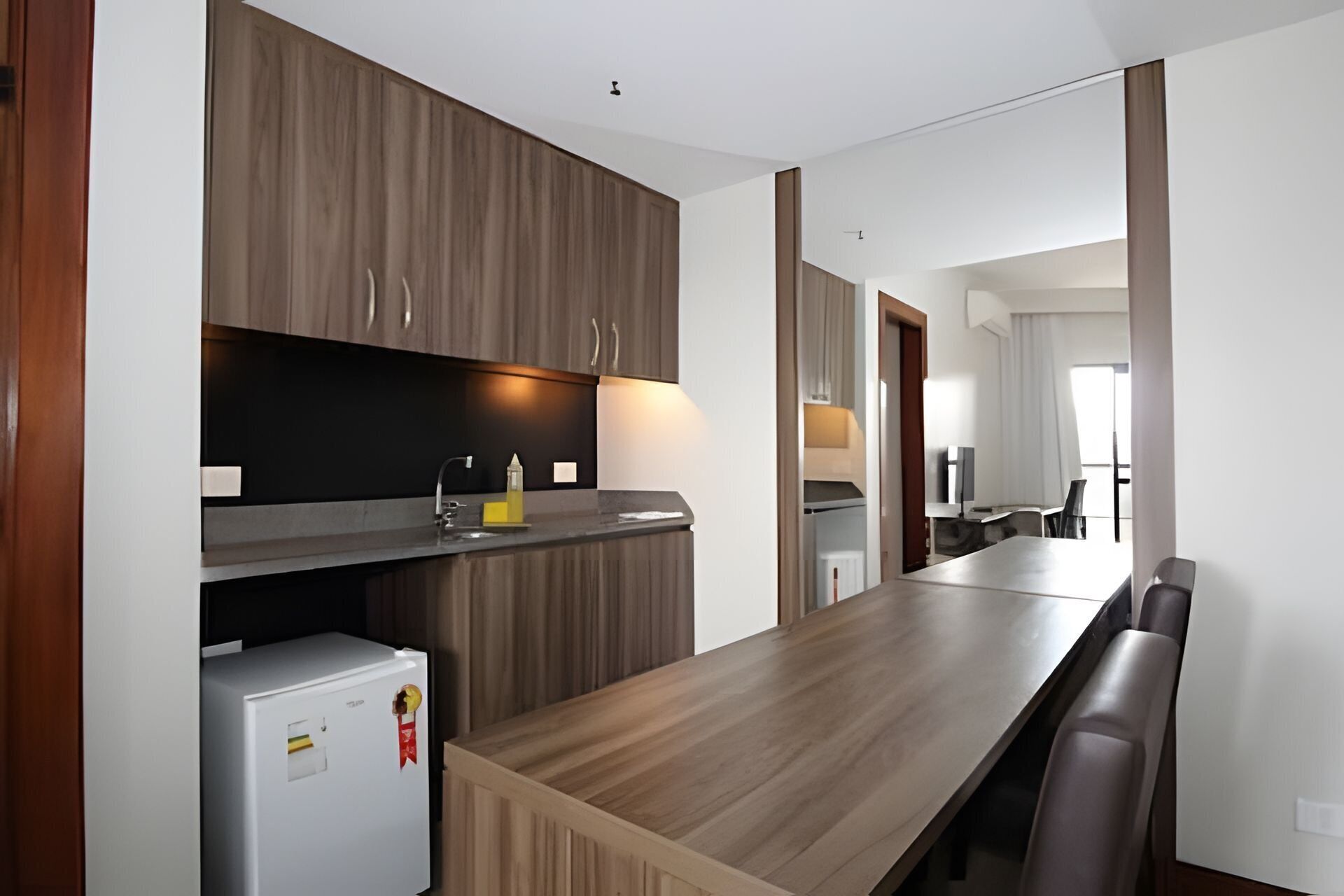 A modern kitchen with wooden cabinets, a built-in refrigerator, and a long dining table with chairs.