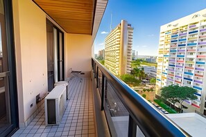 A balcony with a view of a modern building complex, a tiled floor, and a railing.