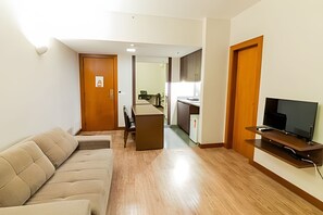 A living room with a sofa, a TV, a wooden floor, and a kitchen in the background. - OZPED Flats Particulares Bonaparte (Brasília)