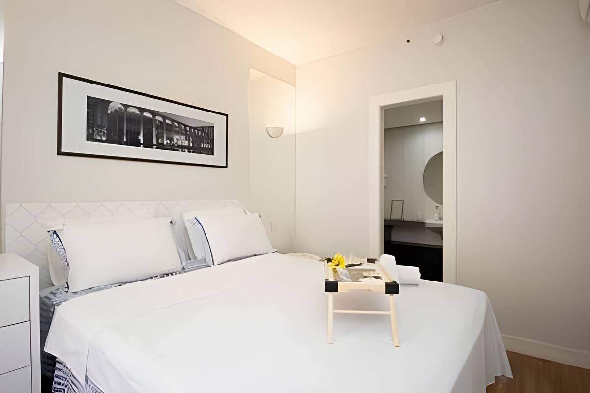 Ein ordentlich eingerichtetes Hotelzimmer mit Bett, Nachttisch mit Lampe, einem gerahmten Bild an der Wand und einer Tür zu einem Badezimmer.
