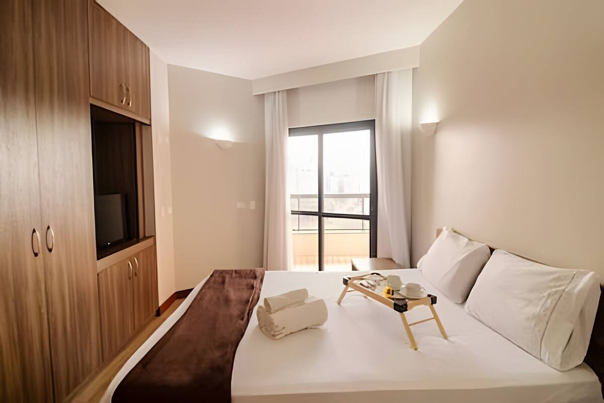 Ein Hotelzimmer mit einem Bett, einem Holzschrank, einem Fenster mit Vorhängen und einem kleinen Tisch mit Tablett.