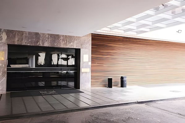 A modern building entrance with a glass door, a concrete wall, and a wooden slatted wall. - OZPED Flats Particulares Bonaparte (Brasília)