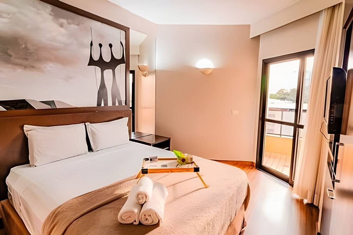 Ein Hotelzimmer mit Bett, Flachbildfernseher, Fenster mit Vorhängen und Wandlampe.