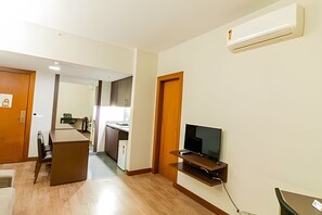 A modern living room with a flat-screen TV, wooden flooring, and a kitchen in the background. - OZPED Flats Particulares Bonaparte (Brasília)