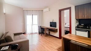 A compact living space with a sofa, a desk, a television, and a kitchenette. - OZPED Flats Particulares Bonaparte (Brasília)