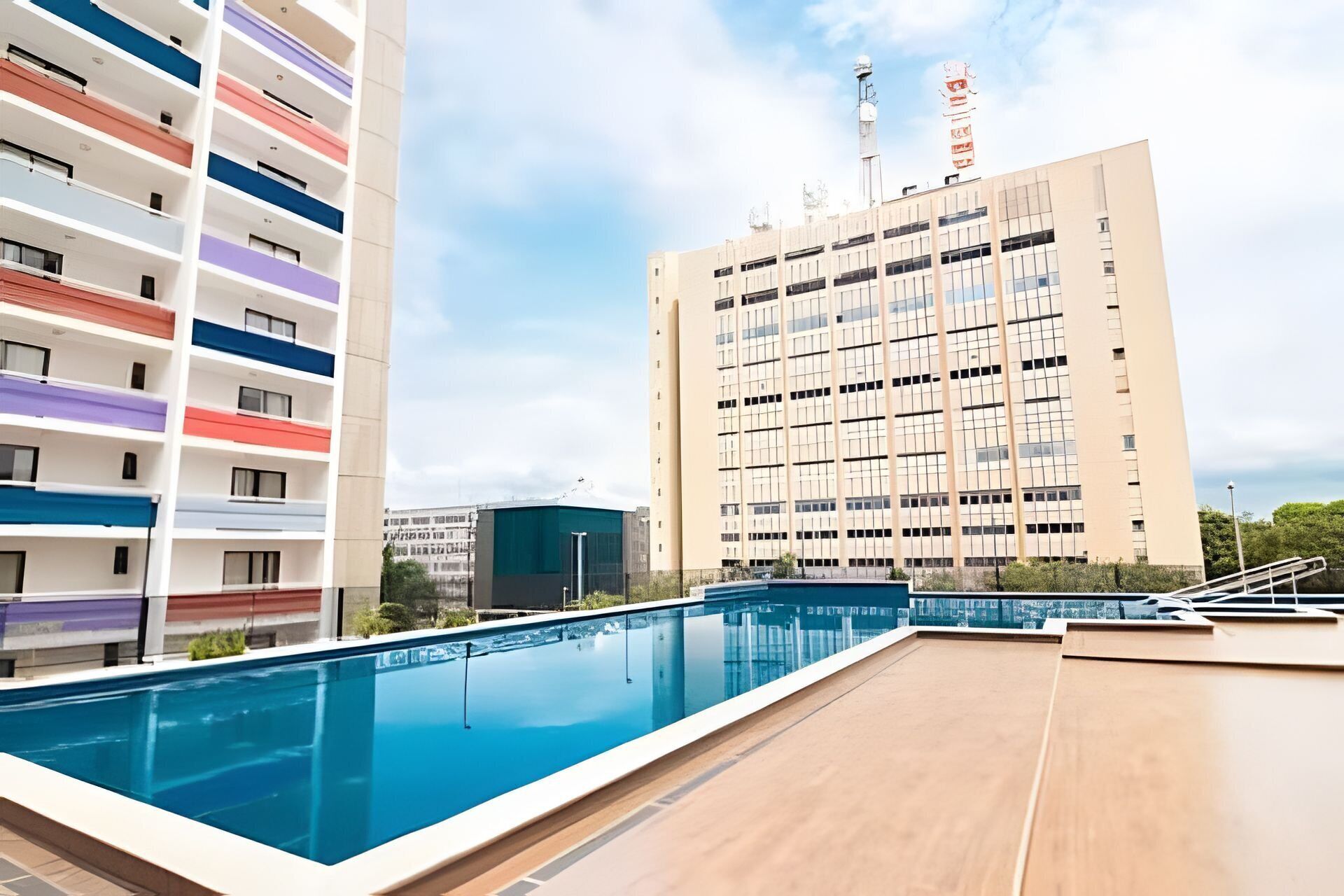 Una piscina en la azotea con vistas a un edificio de varios pisos con balcones.