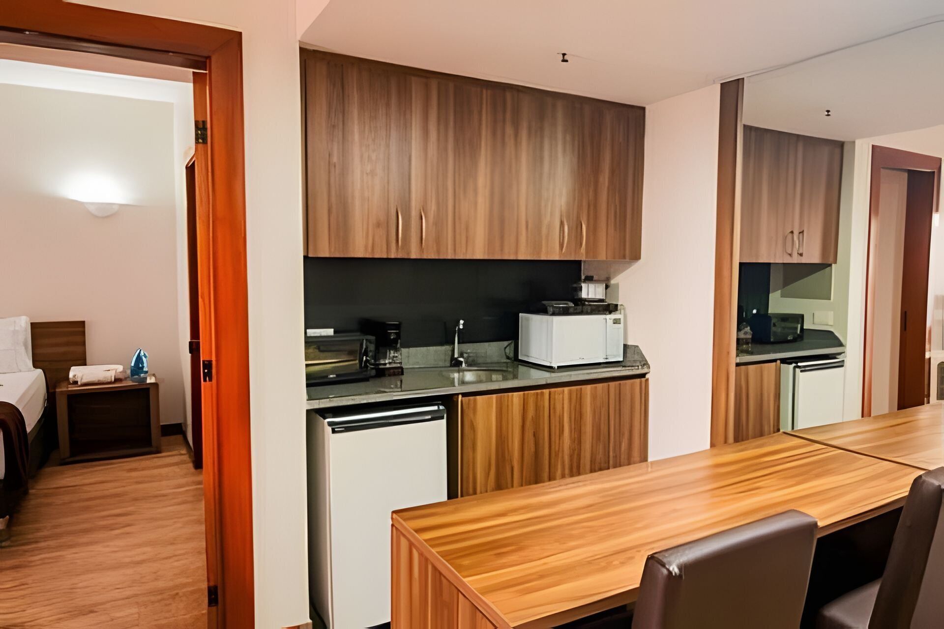 Una habitación de hotel compacta con kitchenette, una mesa de comedor de madera y una cama con mesita de noche.