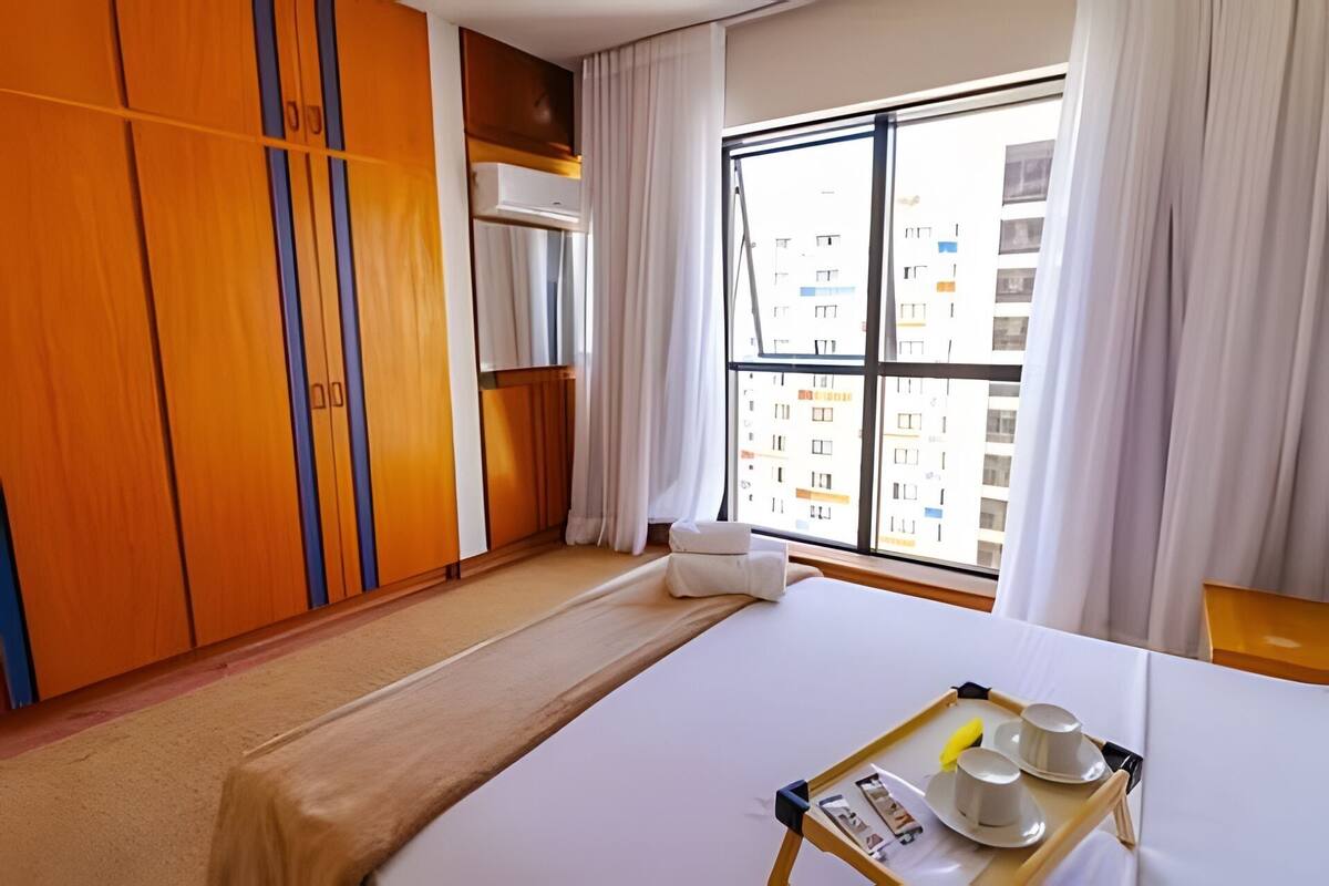 Ein Hotelzimmer mit Bett, einem Vorhangfenster, einem Holzschrank und einem Tablett mit Tassen und einer Banane.
