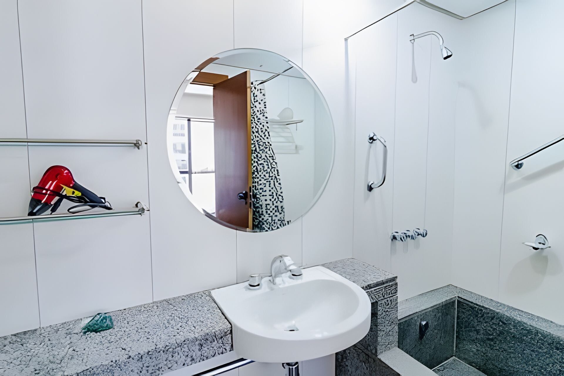Un baño con un espejo redondo, un lavabo, una ducha y un perchero para toallas.