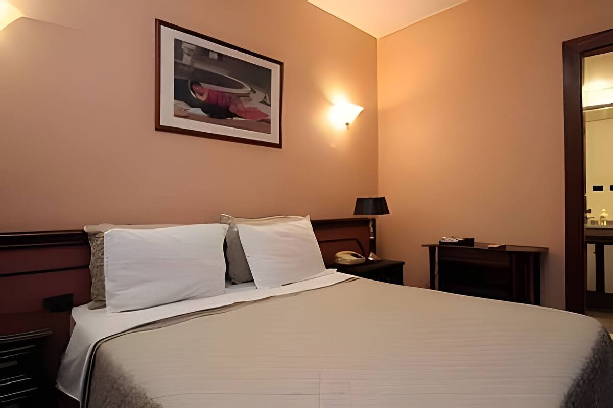 Ein Hotelzimmer mit Bett, Nachttisch, Lampe, gerahmtem Bild an der Wand und Spiegel.