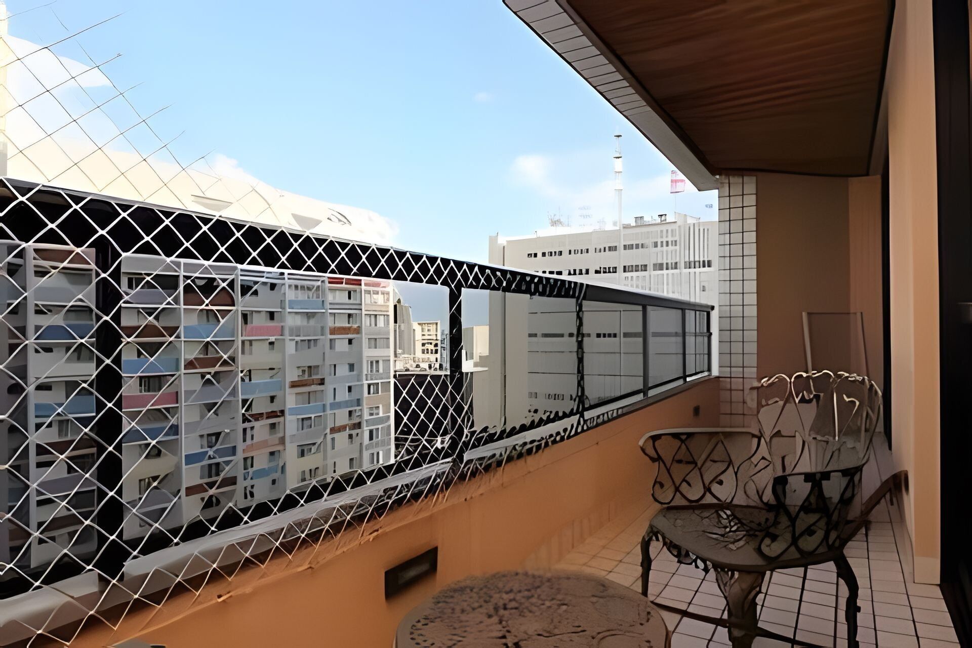 Un balcon avec une balustrade en métal, une chaise et une vue sur les immeubles.