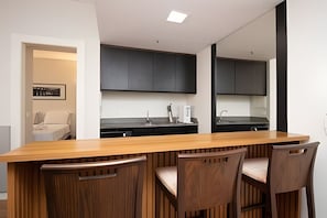 A modern kitchen with dark cabinets, a wooden countertop, and a dining area with three chairs. - OZPED Flats Particulares Bonaparte (Brasília)