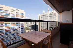 A balcony with a wooden table and chairs, a view of a multi-story building with colorful balconies, and a clear sky. - OZPED Flats Particulares Bonaparte (Brasília)