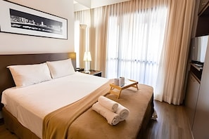 A hotel room with a bed, a nightstand, a lamp, a window with curtains, and a framed picture on the wall.