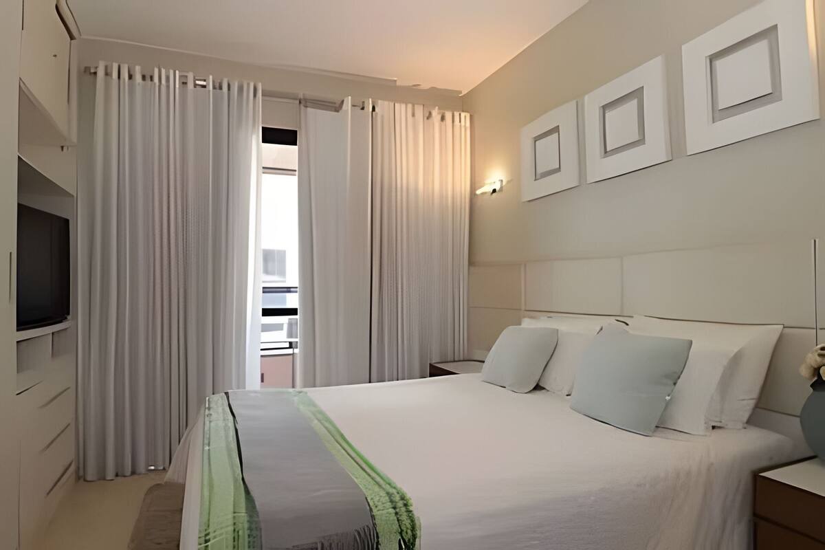 Ein Hotelzimmer mit einem Bett, Vorhängen, einem Fernseher und einer Wandleuchte.