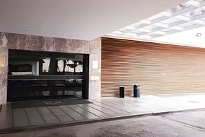 A modern building entrance with a glass facade, a wooden slatted wall, and a metal door. - OZPED Flats Particulares Bonaparte (Brasília)