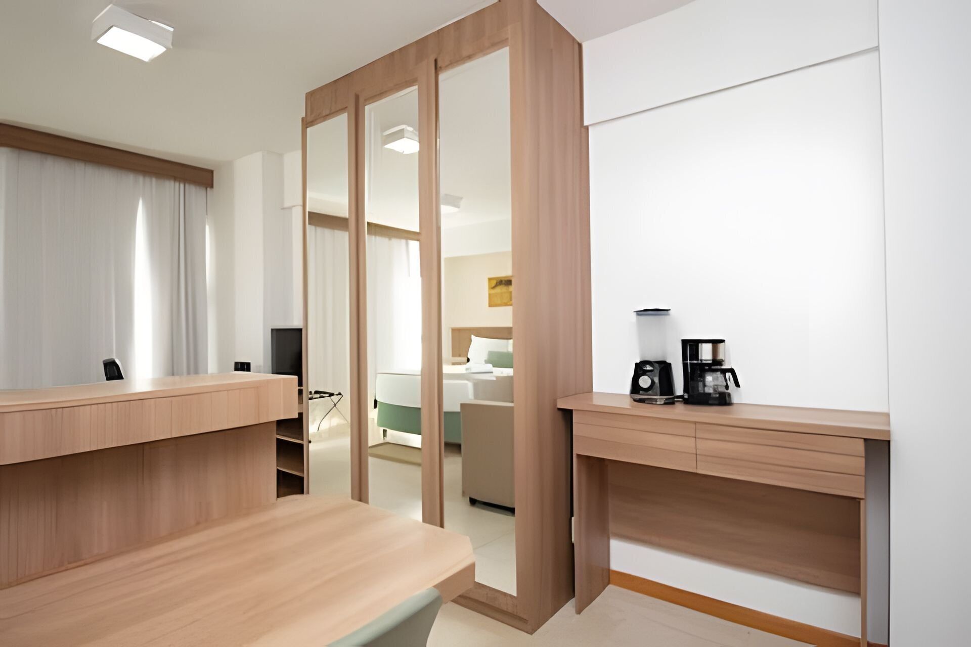 A modern hotel room with a wooden desk, a coffee maker, and a bed with a green headboard.