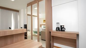 A modern hotel room with a wooden desk, a coffee maker, and a bed with a green headboard.