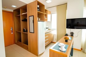 A modern kitchen with wooden cabinets, a built-in refrigerator, a microwave, and a dining area with a table set for two. - OZPED Flats Particulares Saint Moritz (Brasília)