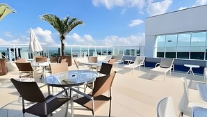 Una terraza en la azotea con mobiliario exterior, una palmera y vistas de la ciudad.
