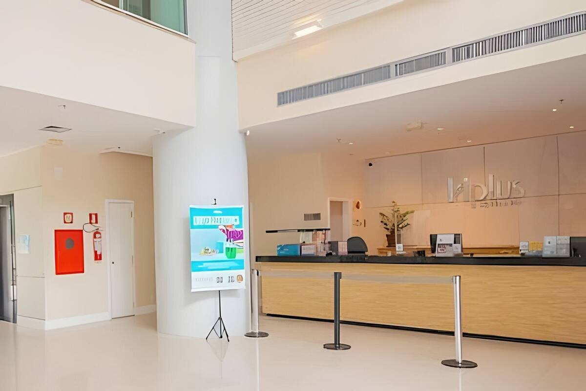 A modern reception desk with a digital screen, a red emergency exit sign, and a white pillar with a poster.