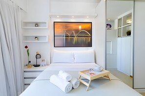 A modern hotel room with a bed, a small bedside table with a tray, a framed picture on the wall, and a view of a bridge. - OZPED Flats Particulares Saint Moritz (Brasília)