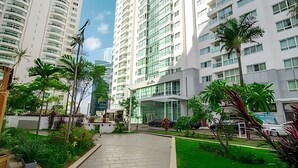 Un edificio residencial moderno de varios pisos, con un patio central con vegetación y un automóvil estacionado en la entrada.