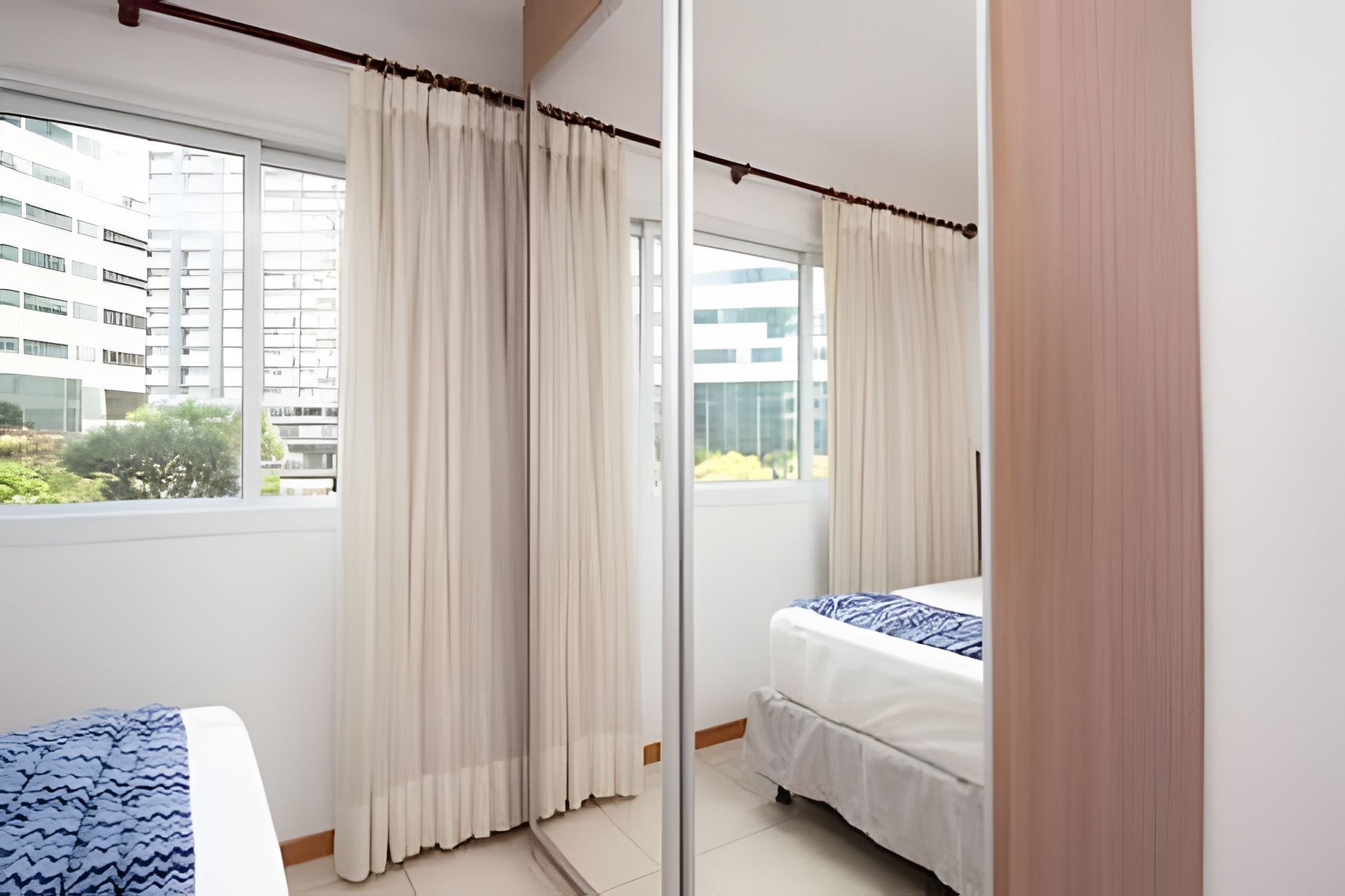 Habitación de hotel con cama, ventana con cortinas y vistas a edificios.