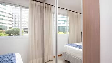 Habitación de hotel con cama, ventana con cortinas y vistas a edificios.