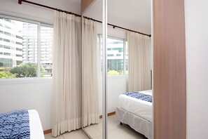 A hotel room with a bed, a window with curtains, and a view of buildings outside.