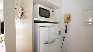 A room with a microwave on top of a white refrigerator, a telephone, and a door with a handle. - OZPED Flats Particulares Saint Moritz (Brasília)
