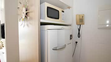 Een kamer met een magnetron bovenop een witte koelkast, een telefoon en een deur met een handvat.