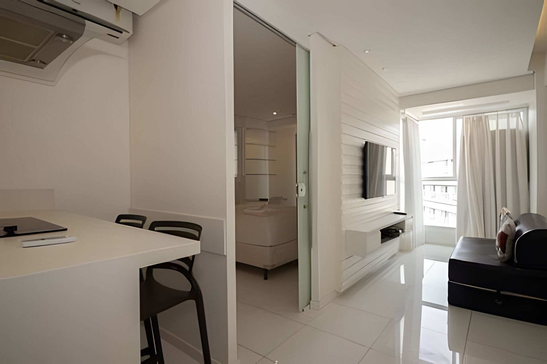 Een moderne, goed verlichte kamer met een eettafel, stoelen, een aan de muur bevestigde televisie en een balkon met gordijnen.