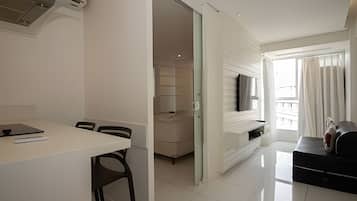 Een moderne, goed verlichte kamer met een eettafel, stoelen, een aan de muur bevestigde televisie en een balkon met gordijnen.