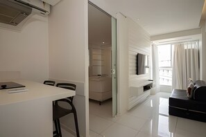 A modern, well-lit room with a dining table, chairs, a TV mounted on the wall, and a balcony with curtains.