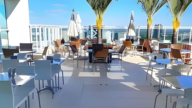 Un área de estar al aire libre con mesas, sillas, sombrillas y vistas de la ciudad.