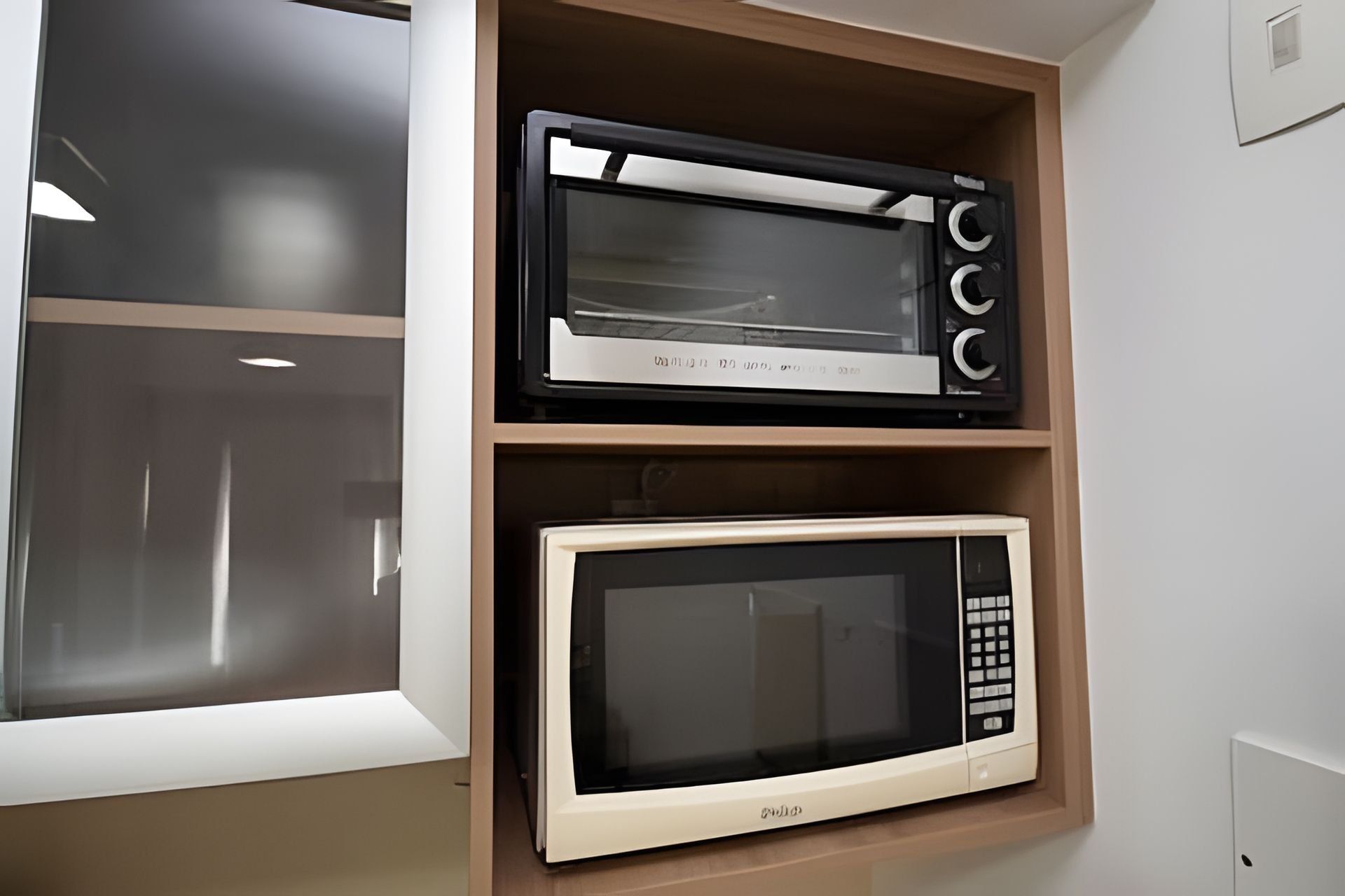 A kitchen with a microwave on the upper shelf and a toaster on the lower shelf.