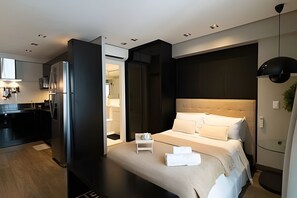 Une chambre d’hôtel moderne dotée d’un grand lit, d’une petite table de chevet, d’un bureau intégré et d’une kitchenette.