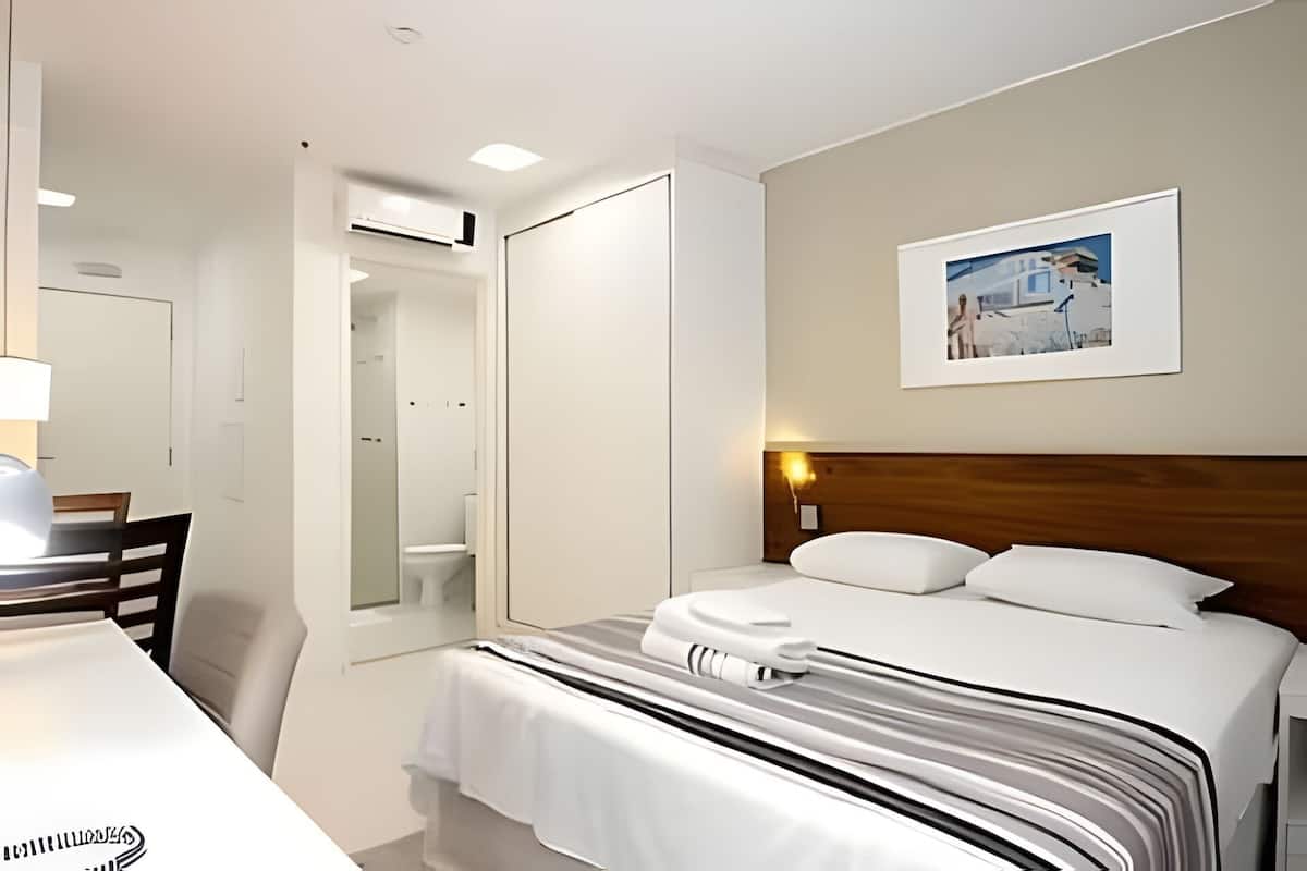 A hotel room with a bed, a desk, a chair, a mirror, and a picture on the wall.