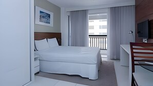 Une chambre d’hôtel avec un lit, un bureau, une chaise, une télévision, un tableau au mur et un balcon avec des rideaux.