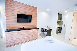 A modern bedroom with a TV mounted on a wooden panel wall, a bedside table, and a chair. - OZPED Flats Particulares Fusion (Brasília)