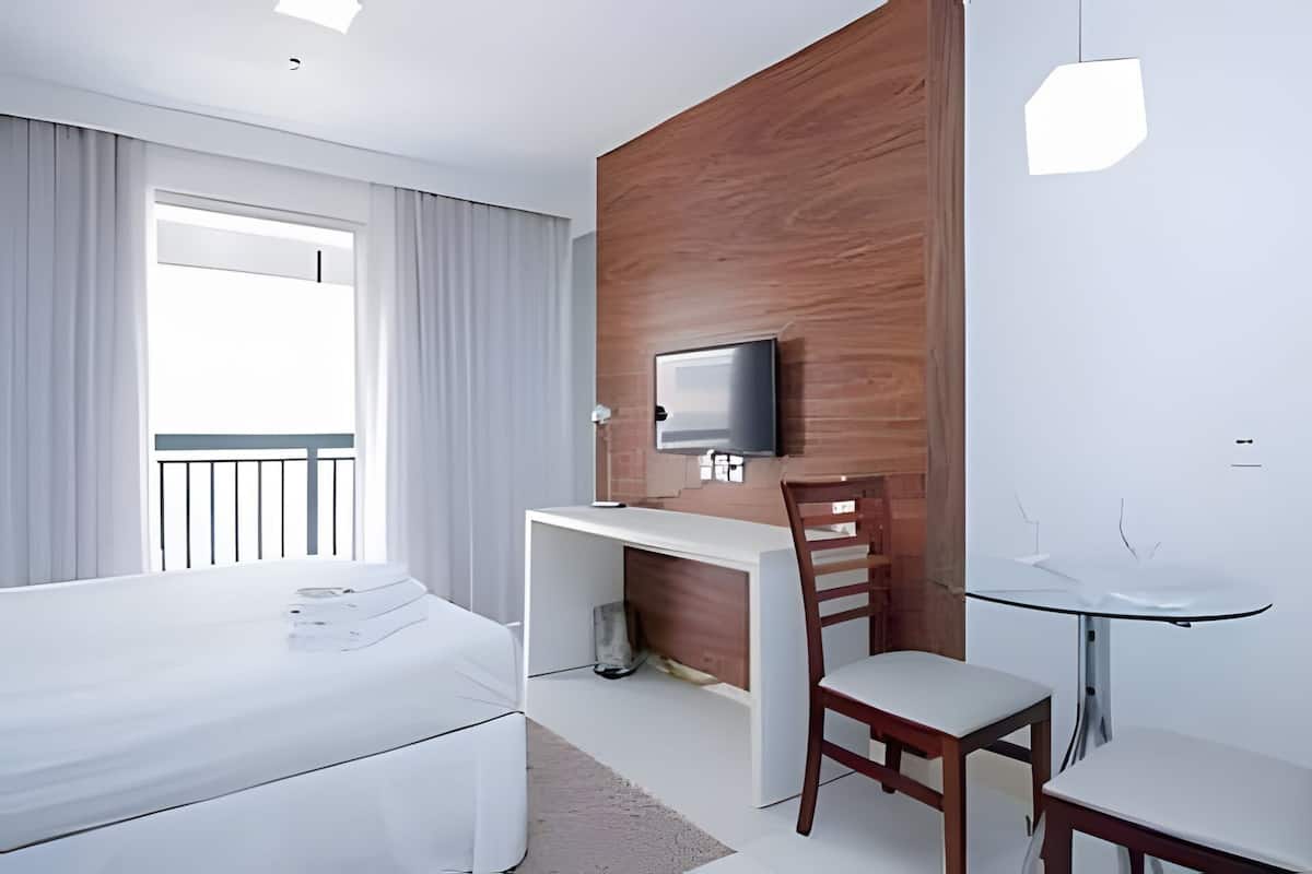 A modern hotel room with a bed, a desk, a chair, a TV, and a glass table.