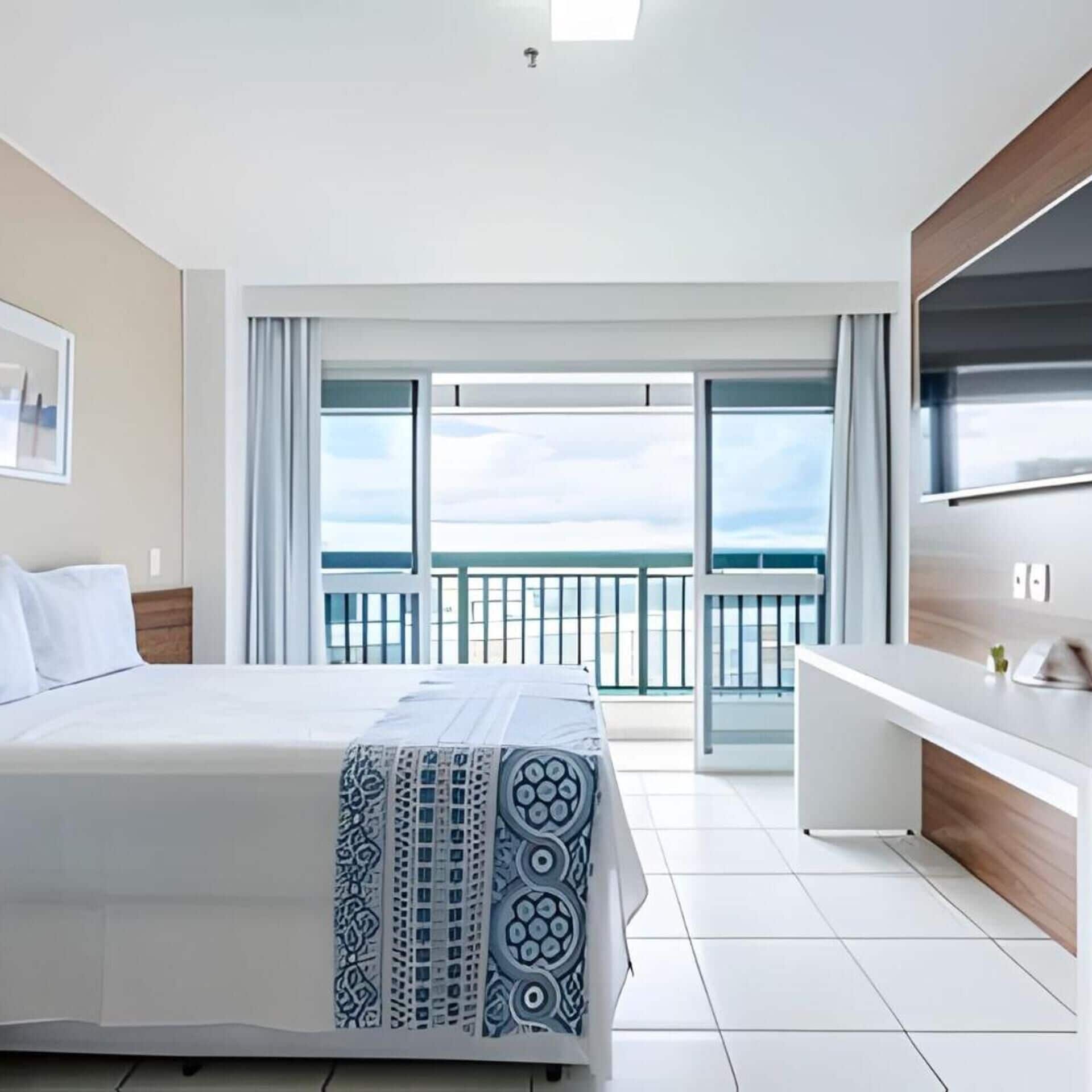 Une chambre d’hôtel avec un lit, une télévision, un bureau et un balcon offrant une vue.