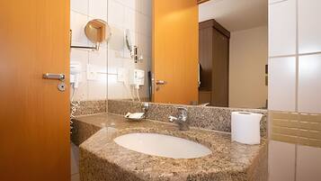 A bathroom with a granite sink, a mirror, a toilet paper dispenser, and a wooden door.