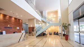 Un hall d’entrée moderne avec un comptoir d’accueil en bois, un escalier et une entrée en verre.