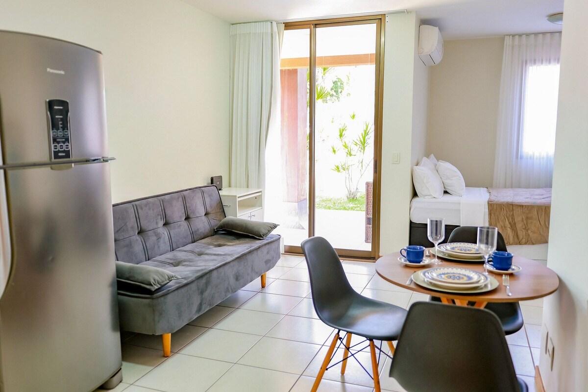 A modern room with a sofa, dining table, chairs, a refrigerator, and a bed with a view.