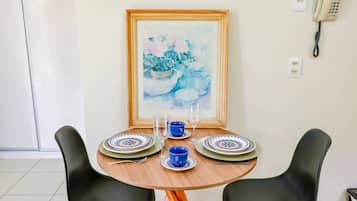 Een eettafel met twee stoelen, een lijst met een schilderij, een telefoon en twee stopcontacten op de muur.